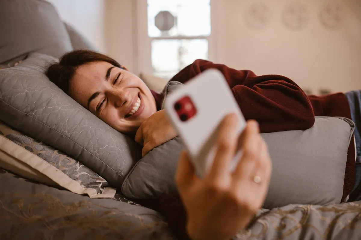 A woman lying on a sofa, smiling at a message on her phone